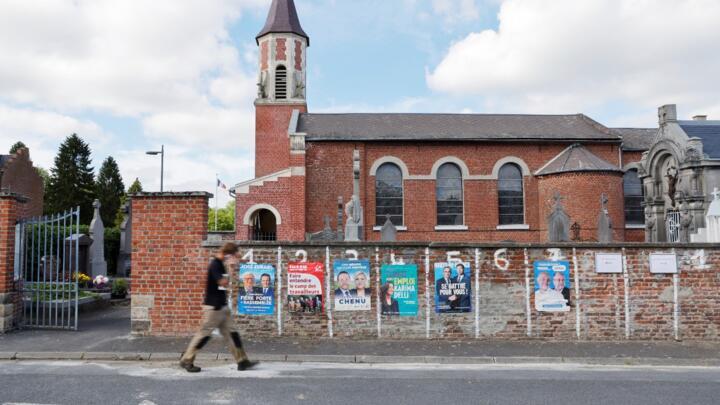 A worker walks past a cemetery's wall used as a panel for election posters ahead of the upcoming French regional elections in Cantin, France, on June 11, 2021.